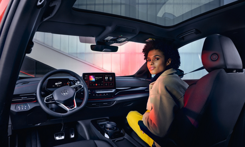 VW ID.4 GTX interior with view of front seats and cockpit. Woman sitting on passenger seat with view to the rear.