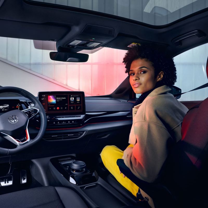 Habitáculo de un VW ID.4 GTX, vista de asientos delanteros y el puesto de conducción. Mujer en el asiento del acompañante mira hacia atrás.