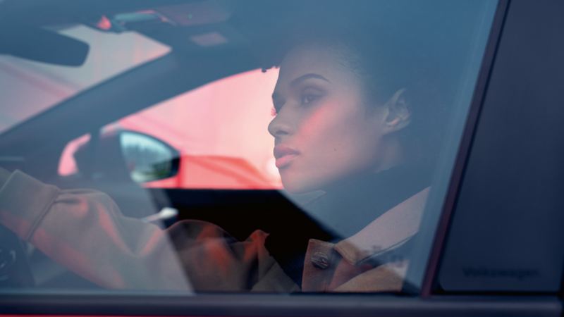 Woman sitting in VW ID.4 GTX on driver's seat with hand on steering wheel looking out.