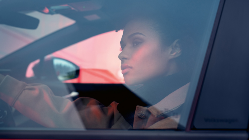 Woman sitting in VW ID.4 GTX on driver's seat with hand on steering wheel looking out.