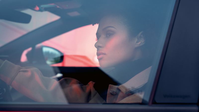 Frau sitzt in VW ID.4 GTX auf Fahrersitz mit Hand auf Lenkrad und schaut raus.
