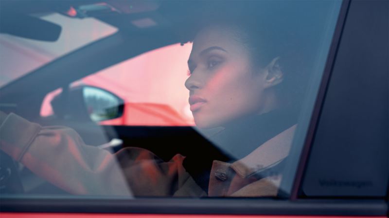 Woman sitting in VW ID.4 GTX on driver's seat with hand on steering wheel looking out.