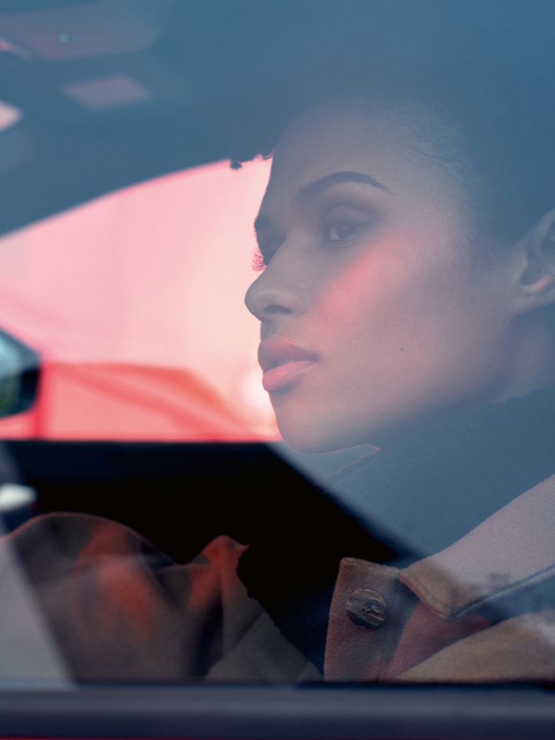 Dans une VW ID.4 GTX, une femme est assise sur le siège conducteur, la main sur le volant et regarde dehors.