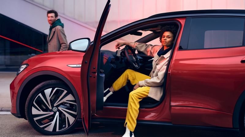 Vue latérale d’une VW ID.4 GTX rouge, portière conducteur ouverte, une femme est assise sur le siège conducteur.