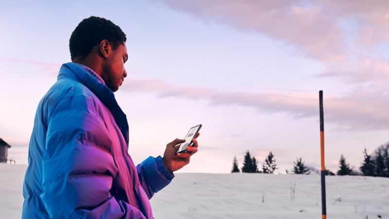 Un homme dans un paysage enneigé regarde sur son smartphone.