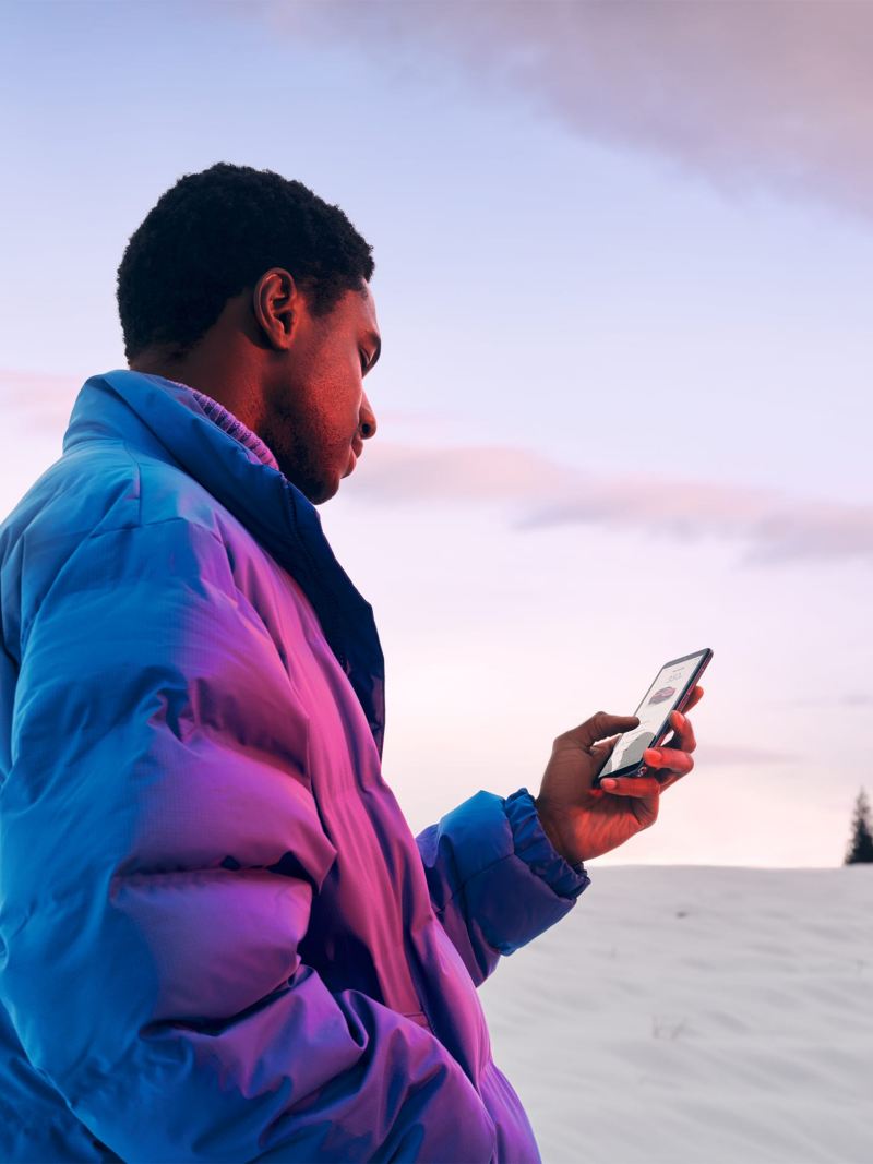 Un hombre con chaqueta de invierno está de pie en un paisaje nevado y mira su móvil.