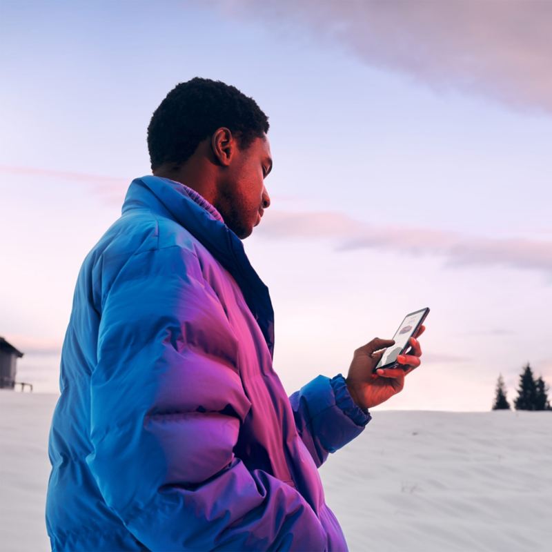 Vyras žiemos peizaže žiūri į išmanųjį telefoną