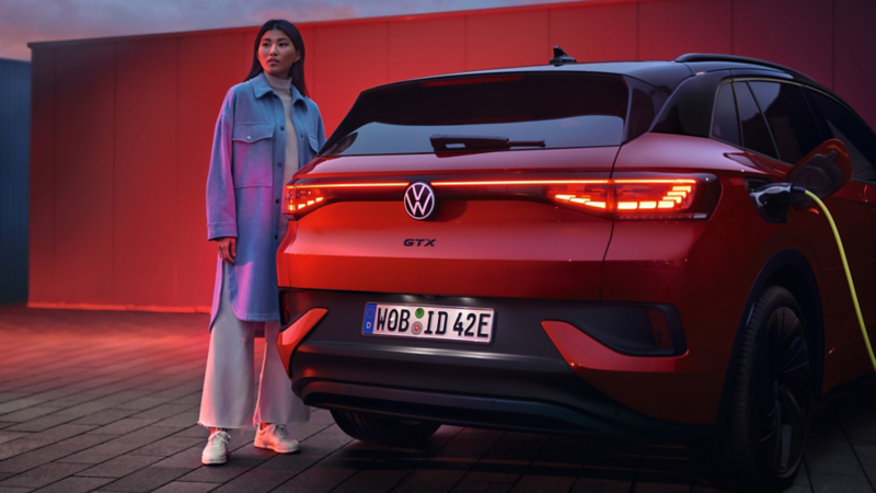 VW ID.4 GTX in Rot von hinten beim Laden. Frau steht daneben.