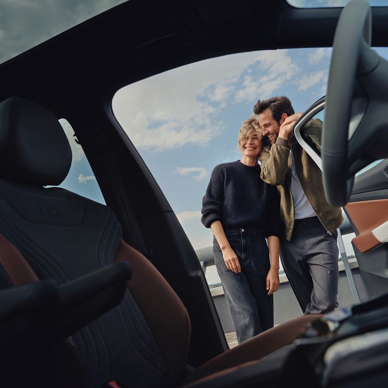 Blick vom Beifahrersitz des VW ID.4 auf Fahrertür. Paar steht an offener Tür und lacht.