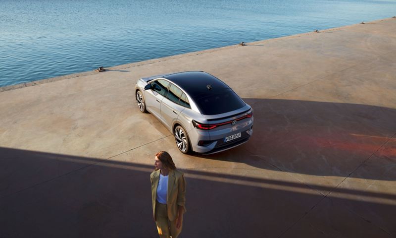 Rear view of a VW ID.5 at a harbor quay, view from diagonally above, a woman stands in the foreground