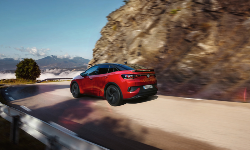 Ένα κόκκινο VW ID.5 GTX κινείται δυναμικά σε ορεινό δρόμο. Άποψη στο πλαϊνό μέρος, στους τροχούς και στο πίσω μέρος.