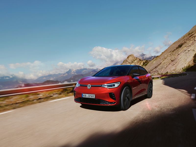 Roter VW ID.5 GTX fährt dynamisch auf einer Bergstraße. Blick auf Front, Räder und Seite.
