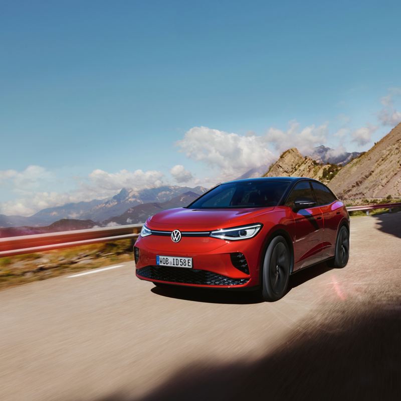Roter VW ID.5 GTX fährt dynamisch auf einer Bergstraße. Blick auf Front, Räder und Seite.