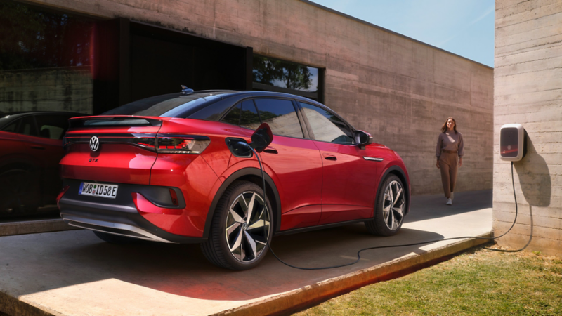 Sarkans VW ID.5 GTX ir novietots pie modernas mājas un tiek uzlādēts ar ID. Charger, vīrietis tuvojas automašīnai