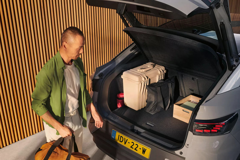 Een man wil een tas in de kofferbak van een Volkswagen ID.5 stoppen, de kofferbak staat open en je ziet al wat spullen die zijn ingeladen
