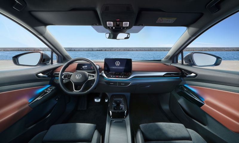 Άποψη στο εσωτερικό ενός VW ID.5 στο σκοτάδι, άποψη από το μπροστινό κεντρικό υποβραχιόνιο, το τιμόνι, την οθόνη Infotainment και τον φωτιζόμενο με ροζ χρώμα πίνακα οργάνων. Η οθόνη δείχνει τις ρυθμίσεις του φωτισμού Ambiente. 