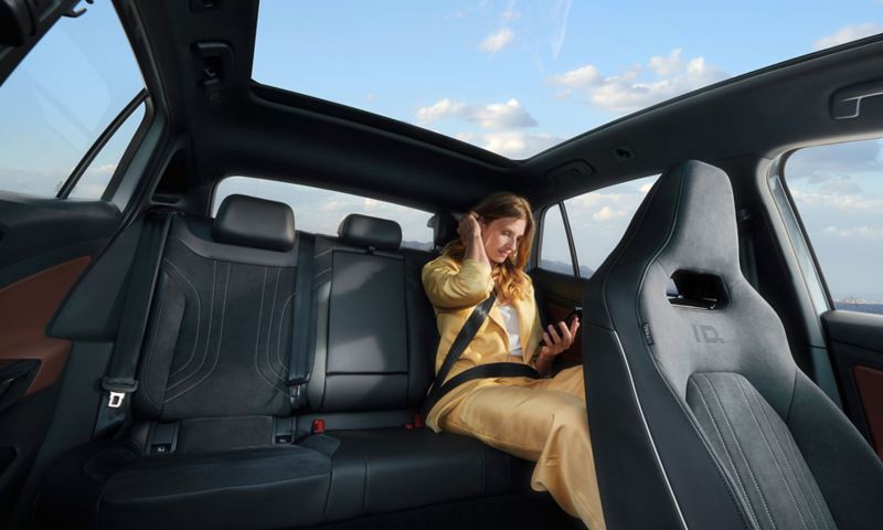 Interior view of a VW ID.5, front view of the back seat on which a reading woman is sitting 