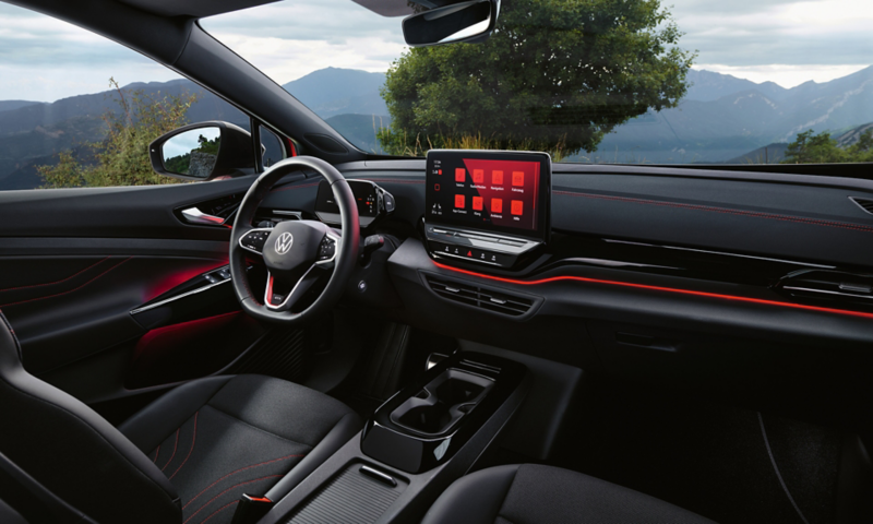 Εσωτερικός χώρος ενός κόκκινου VW ID.5 GTX στο σκοτάδι. Άποψη από το τιμόνι, την οθόνη Infotainment και τον, φωτιζόμενο με κόκκινο χρώμα πίνακα οργάνων. 