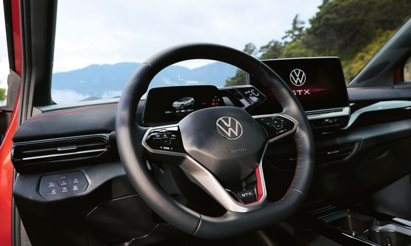En rød VW ID.5 GTX indefra. Blik på rattet, instrumenterne og displayet. Forbundet med den stemmestyrede assistent.
