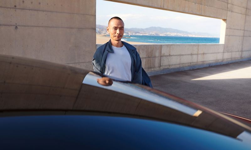 Junger Mann steht lächelnd hinter einem blauen VW ID.5, der in einem Gebäude parkt.