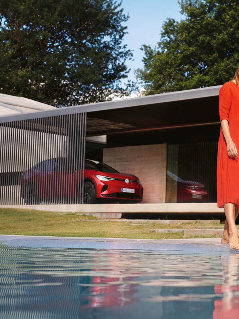 Een rode VW ID.5 GTX wordt voor een huis geparkeerd. Een vrouw in een rode jurk aan het zwembad.