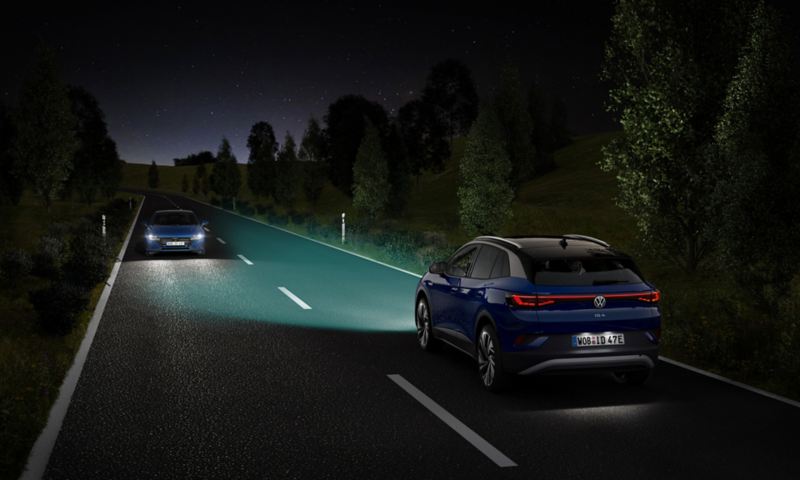 Ein blauer VW ID.4 fährt mit eingeschaltetem Licht eine nächtliche Straße entlang.