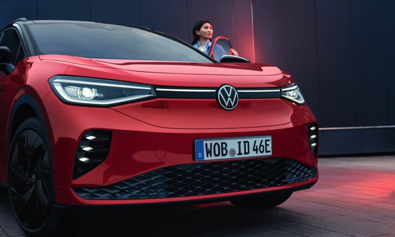 VW ID.4 GTX in Rot mit geöffneter Fahrertür. Frau steht an der Tür und guckt nach vorne.