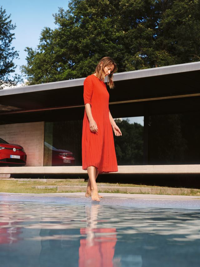 Roter VW ID.5 GTX parkend vor einem Haus. Eine Frau im roten Kleid am Pool.