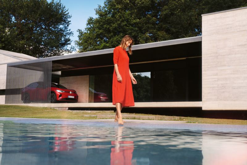 Roter VW ID.5 GTX parkend vor einem Haus. Eine Frau im roten Kleid am Pool.