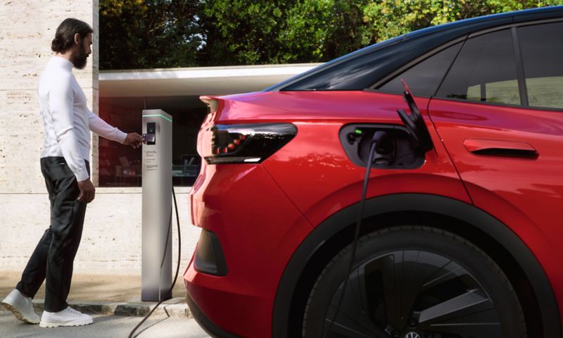 Red VW ID.5 GTX in exterior coupé design in front of a house. Connected to a charging station by cable.