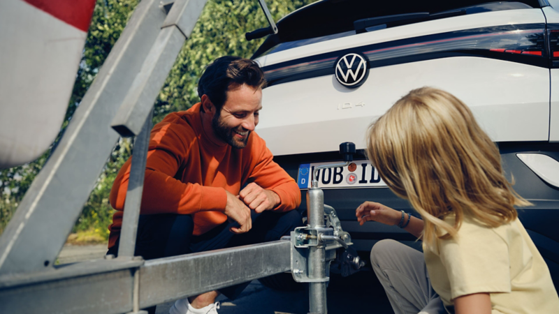 Detailed view of crouching man and young girl at the towing bracket of VW ID.4. 