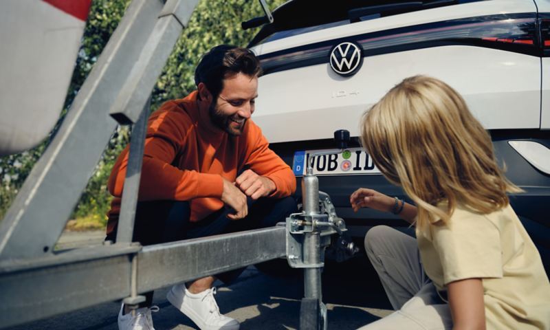 Detailopname van een man op zijn hurken en een klein meisje bij de trekhaak van de VW ID.4. 