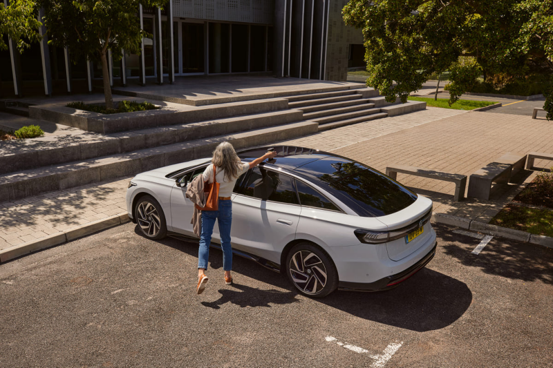 Vrouw haalt een mok van het dak van een geparkeerde witte Volkswagen ID.7