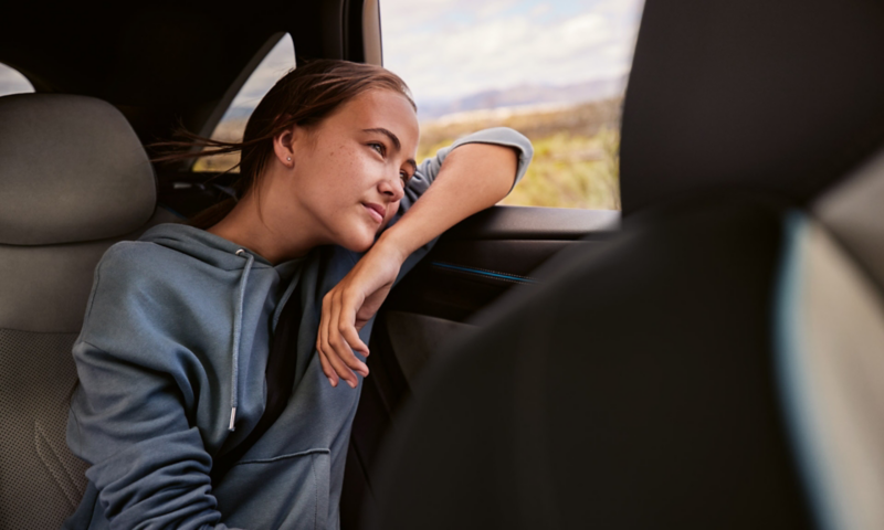 Młoda kobieta na tylnym siedzeniu VW ID.7, patrzy przez okno na zewnątrz.