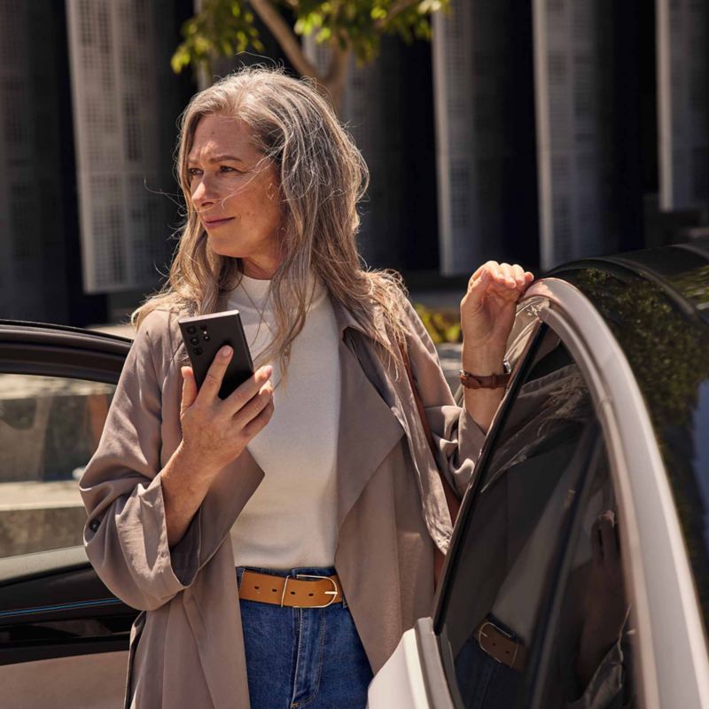 Donna con uno smartphone in mano vicina ad una Volkswagen.