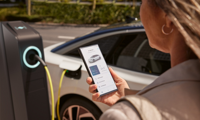 A woman stands in front of the ID.7 holding her phone in her hand, on which she can check the charge level.