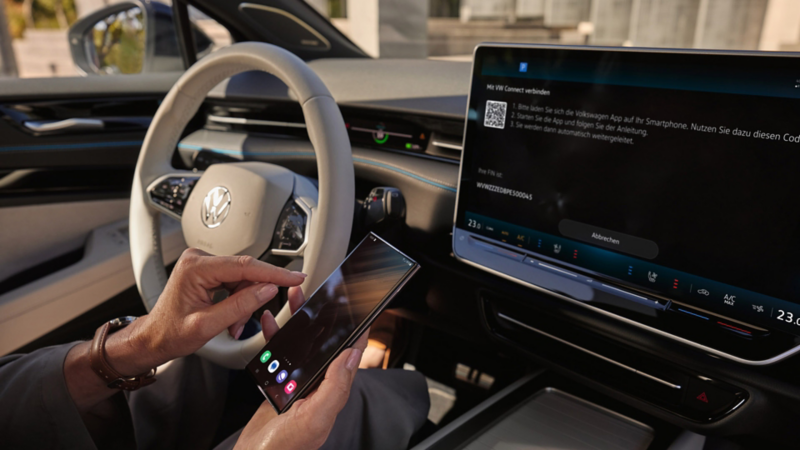 Man in a Volkswagen car connects a smartphone to the vehicle's touchscreen display, showcasing smart technology.