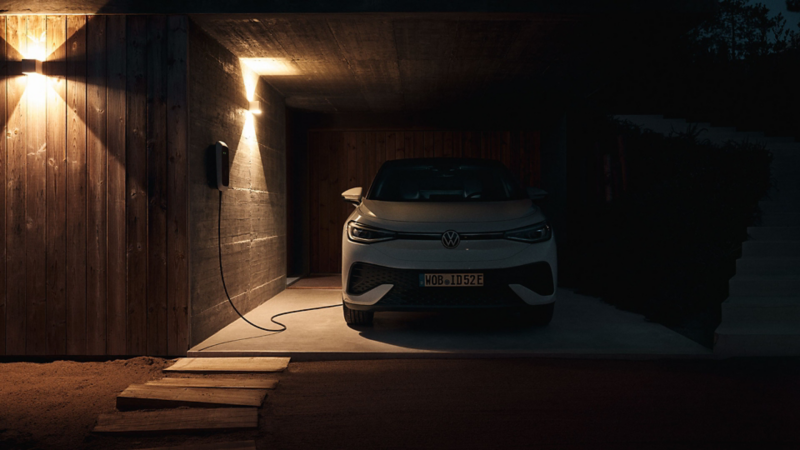 Ein VW ID.5 Pro lädt nachts an einer Wallbox vor einem Haus mit warmem Licht.
