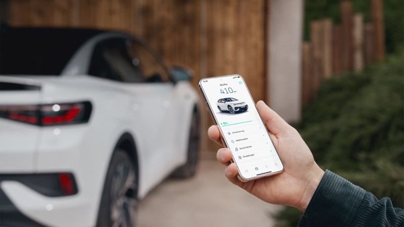 En person står intill en Volkswagen och använder Volkswagen-appen på en mobiltelefon