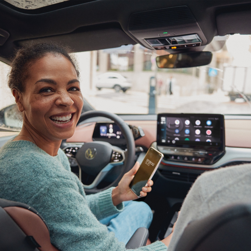 Une femme au volant d'une Volkswagen ID.3 tient sont téléphone dans sa main avec le système d'infodivertissement du véhicule allumé.