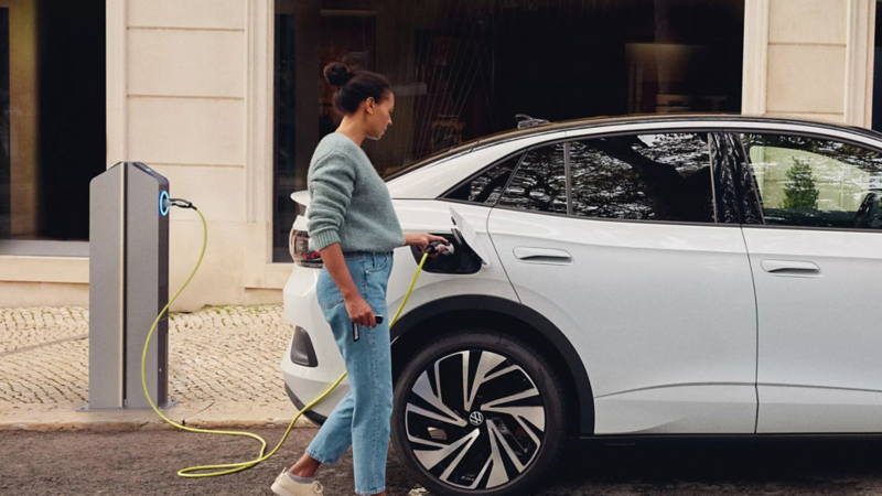 Vrouw steekt oplaadstekker bij een laadpaal in een witte Volkswagen ID.5