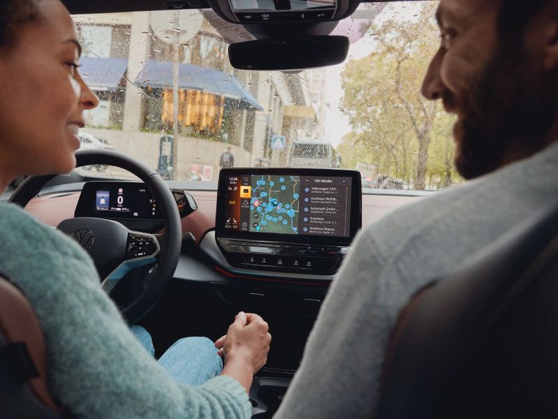 Eine Frau und ein Mann sitzen in einem VW ID.5 und schauen auf das Display des Navis. Angezeigt wird die VW Händlersuche.