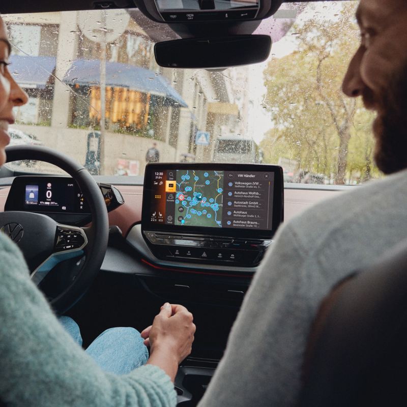 Eine Frau und ein Mann sitzen in einem VW ID.5 und schauen auf das Display des Navis. Angezeigt wird die VW Händlersuche.
