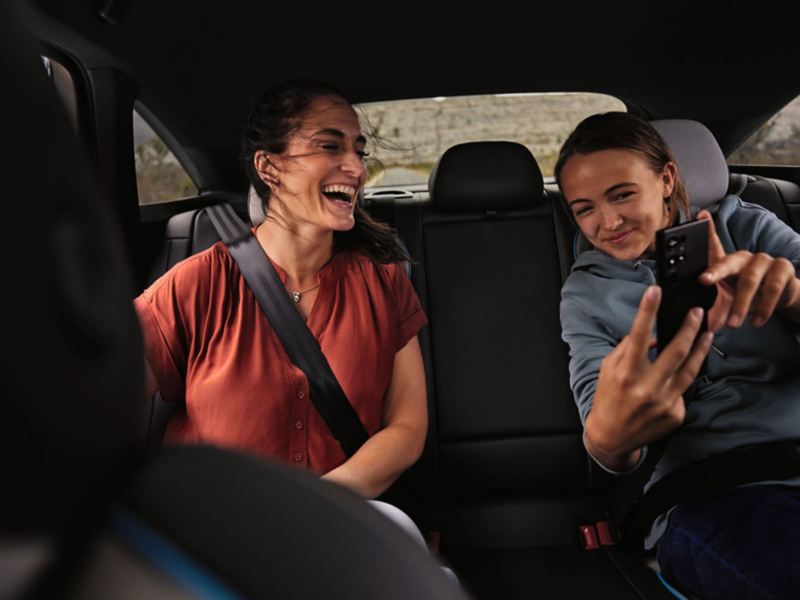 Eine Frau und ein Kind sitzen auf der Rückbank des VW ID.7 und schauen auf ein Smartphone.