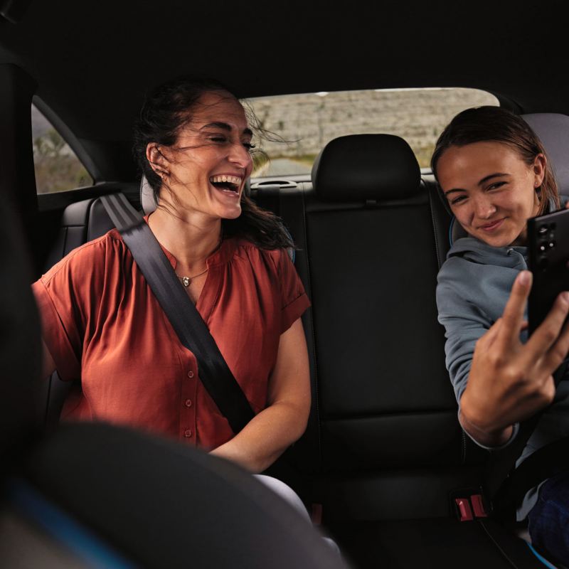 Eine Frau und ein Kind sitzen auf der Rückbank des VW ID.7 und schauen auf ein Smartphone.