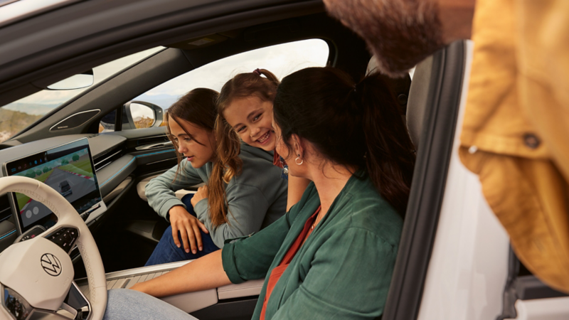 Une famille est assise à bord de la VW ID.7 et l’une des filles regarde l’écran du système d’info-divertissement sur lequel se déroule un match. 