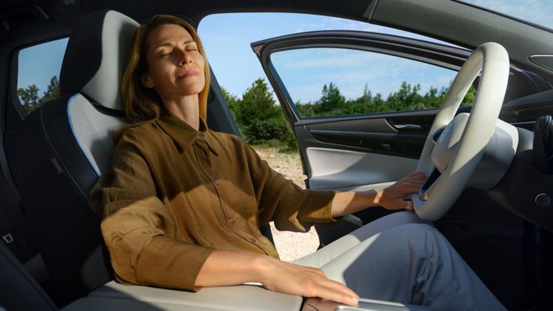 En person sidder ved en åbnet dør i en ID.7 og nyder Wellness In-Car-appen med lukkede øjne 