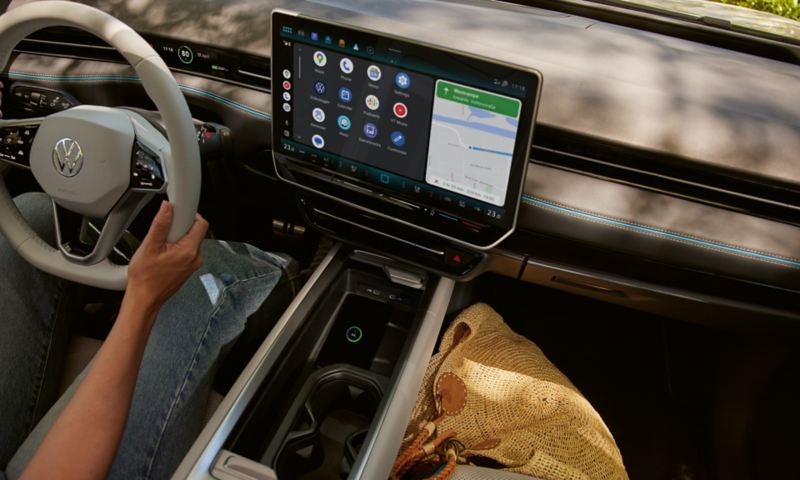 Widok z tylnych siedzeń VW ID.7 do przodu. Kobieta na fotelu kierowcy trzyma w ręku smartfon i łączy się bezprzewodowo przez App Connect.