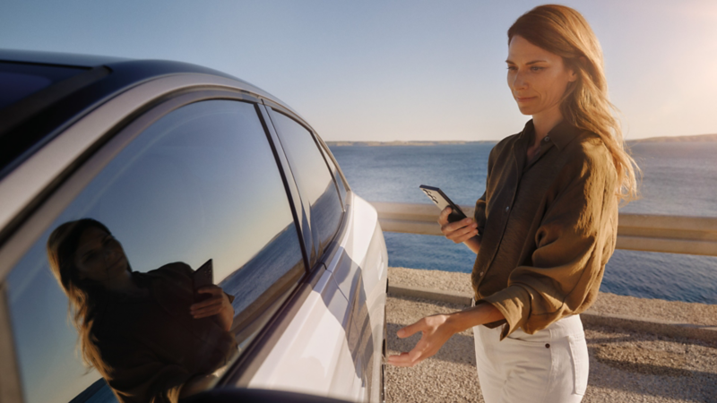 Eine Frau mit Smartphone in der Hand öffnet die Fahrertür eines weißen VW ID.7.