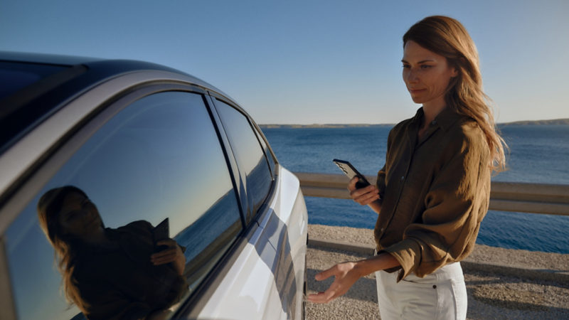 Kobieta trzymająca smartfon w ręku otwiera drzwi kierowcy białego VW ID.7.